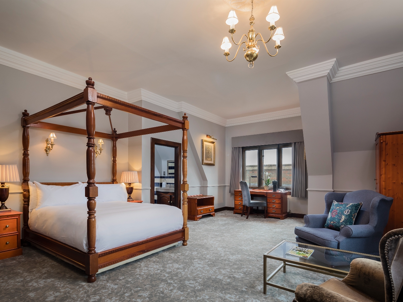 wooden four-poster bed in bedroom suite with grey walls and blue armchair