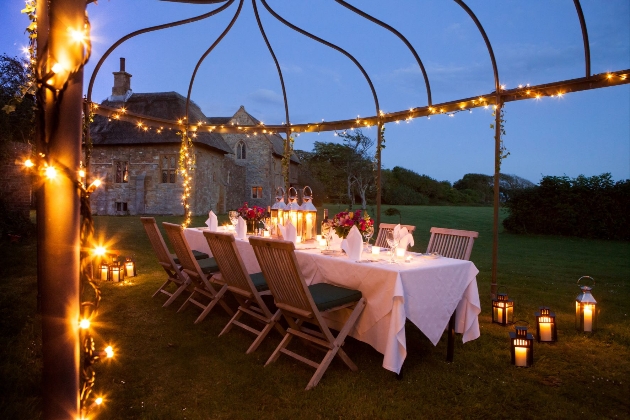 Bailiffscourt gardens at dusk with fairylights, lanterns, and set up for a meal for eight