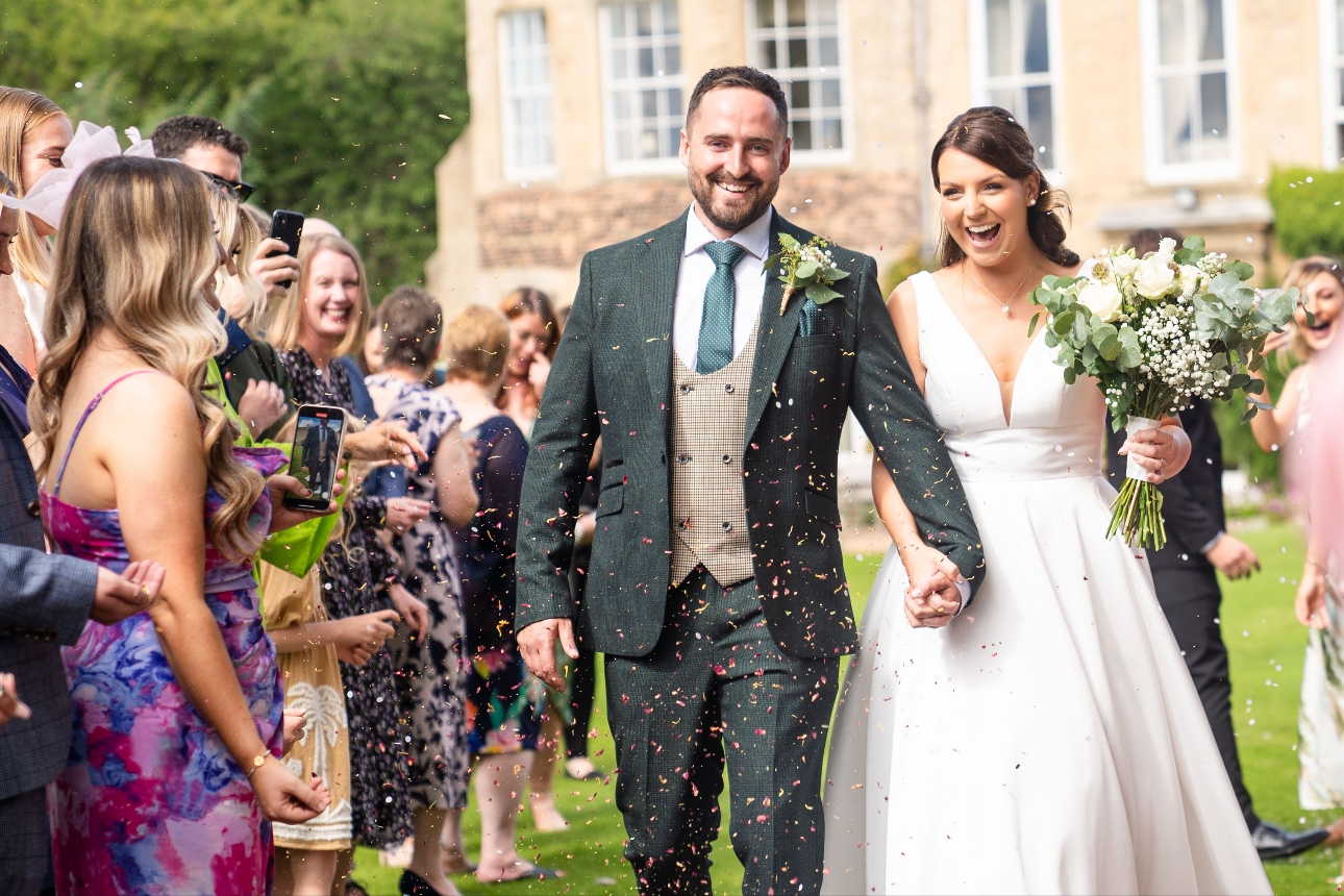 couple on their wedding day leaving venue confetti shot. 